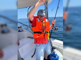 A man proudly displays his catch while fishing aboard a boat, showcasing the excitement of a successful fishing trip on the open water.