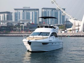 A sleek yacht cruising in calm waters, with modern buildings and a Ferris wheel in the background, perfect for showcasing luxury boating experiences.
