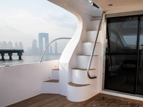 A stylish interior view showcasing the elegant staircase of a yacht, leading to the upper deck with a backdrop of a city skyline.