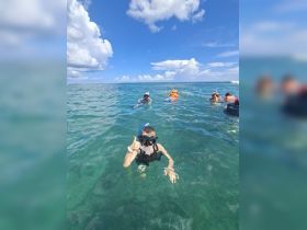 A child gives a thumbs up while snorkeling in clear ocean waters, surrounded by fellow snorkelers — a perfect moment of underwater adventure and fun.