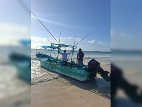 Two fishermen proudly pose with their fishing rods on a small boat at the beach, capturing the essence of a fun fishing adventure on the ocean.