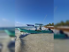 A fishing boat named 'Yazmin' approaches the shore with crew members on board, showcasing a vibrant beach scene perfect for fishing adventures.