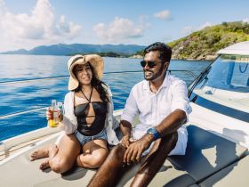 A couple enjoys a sunny day on a boat, sipping drinks and relaxing amidst stunning ocean views — perfect for a romantic getaway.