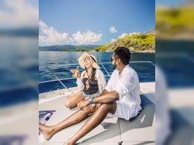 A joyful couple enjoys drinks on the deck of a boat under the sun, perfect for a relaxing day on the water.