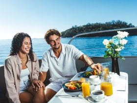 A couple enjoys a delightful breakfast on a yacht, surrounded by stunning ocean views — perfect for romantic getaways or special celebrations.