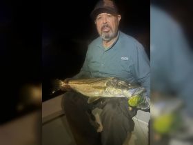 A proud angler displays a large striped bass caught during a night fishing trip, showcasing the thrill of fishing adventures on the water.