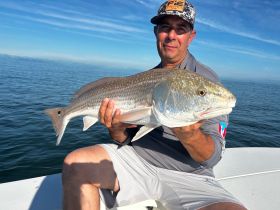 A proud angler displays a freshly caught redfish while out on the water, showcasing the thrill of fishing adventures.