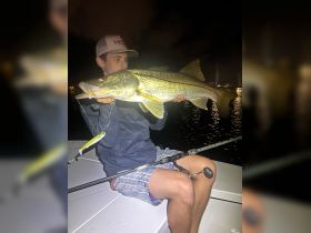 A young angler proudly displays a large catch during a night fishing trip, showcasing the thrill of fishing adventures on the water.