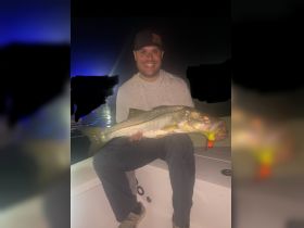 A proud angler displays a large catch during a night fishing trip, showcasing the thrill of fishing adventures on the water.