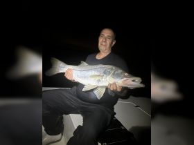 A proud angler displays a large snook caught during a night fishing trip, showcasing the thrill of fishing adventures on the water.