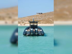 A sleek speedboat is docked in clear turquoise waters, with sunbathers visible on the beach in the background, creating a perfect scene for a day of relaxation and adventure.