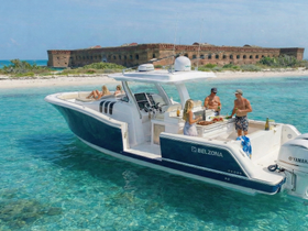 A lively group enjoys a fun day on a Belzona boat, preparing food and drinks while anchored in crystal-clear waters near a historic fort — perfect for memorable outings and celebrations.