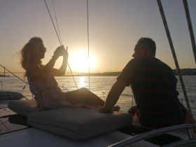 A couple enjoys a romantic sunset on a sailboat, capturing the moment with a photo — perfect for memorable sailing experiences.