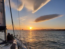 A serene sunset view from a sailboat, with guests enjoying the picturesque scenery as the sun sets over the horizon — an ideal moment for romantic sailing trips.