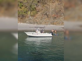 A group enjoys a day at the beach with a boat anchored nearby, showcasing a fun swimming experience in the clear waters.