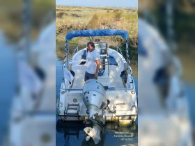 A man stands at the helm of a small boat, showcasing the interior layout with seating and navigation equipment — perfect for exploring coastal waters.