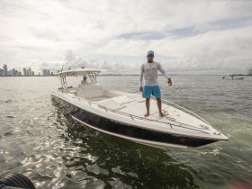 A man stands confidently on the bow of a boat navigating through waters with a vibrant city skyline in the background, showcasing an adventurous day on the water.