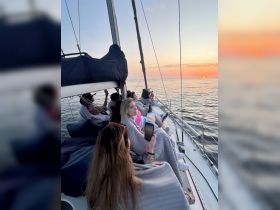 A group of friends enjoys a beautiful sunset while wrapped in blankets on a sailing trip, capturing the essence of relaxation and camaraderie on the water.