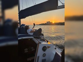A guest relaxes on the deck of a sailboat, capturing the stunning sunset over the water — a perfect moment for unwinding during a scenic cruise.