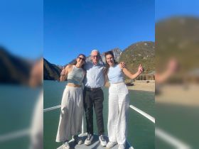 A cheerful group poses on a boat with stunning mountain scenery in the background, capturing a memorable moment on the water.