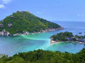 A stunning aerial view of a tropical island with a beautiful coastline and beach, showcasing visitors enjoying the serene waters and lush greenery — a perfect destination for island hopping adventures.