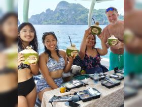 A cheerful group enjoys refreshing coconut drinks aboard a boat, surrounded by stunning scenery — perfect for a fun day on the water.