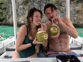 A couple enjoys refreshing coconut drinks while relaxing on a boat, surrounded by beautiful turquoise waters — a perfect moment for beach lovers and adventure seekers.