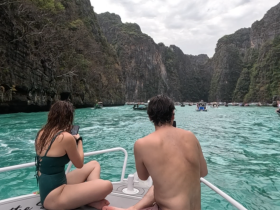 A couple enjoys a scenic boat ride through turquoise waters surrounded by stunning cliffs, capturing the beauty of their adventure on their devices.
