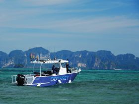 The 'Odyssey' speedboat navigates through clear turquoise waters, showcasing its sleek design against a stunning island backdrop — perfect for fishing or leisure trips.