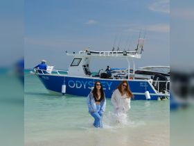 Two friends enjoy a fun day at the beach, splashing in the water near the ODYSSEY boat — a perfect setting for memorable adventures on the water.