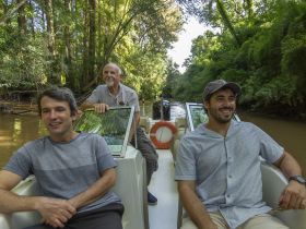 A group of three men enjoys a scenic boat ride through a lush river environment, perfect for nature exploration and adventure.