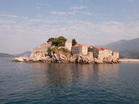 A picturesque view of a charming island with historic stone buildings, surrounded by tranquil waters and mountains — an ideal destination for scenic boat tours.