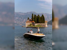Two men enjoy a scenic boat ride near a picturesque island with lush greenery and mountains in the background, perfect for exploring the stunning coastline.