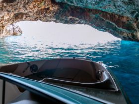 A stunning view from inside a boat looking out of a cave, showcasing the vibrant blue waters and rocky formations — perfect for exploring hidden gems on the water.