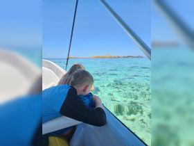Two children gaze over the side of a boat, captivated by the clear turquoise waters and vibrant underwater scenery, perfect for snorkeling adventures near the island.