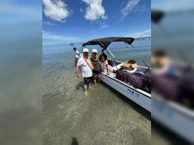 A joyful group poses by their boat in shallow waters, adorned with leis, capturing a memorable beach day filled with family fun and celebration.