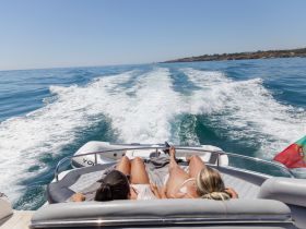 Two friends relax on the deck of a boat, enjoying the sunny ocean views and the thrill of cruising through the waves — a perfect day on the water.