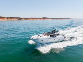 A stylish yacht named 'YOLO1' cruises through clear waters, with guests enjoying the ride against a stunning coastal backdrop.