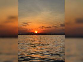 A stunning sunset over a tranquil harbor, with silhouettes of boats dotting the water — perfect for capturing the serene beauty of evening on the water.