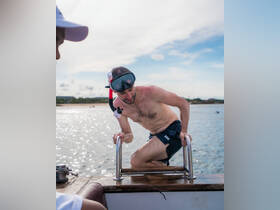 A man prepares to snorkel as he climbs aboard a boat, showcasing the excitement of on-water adventures and marine exploration.