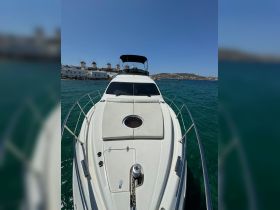 A clear view of a yacht's bow, showcasing its sleek design against a backdrop of turquoise waters and distant windmills — perfect for luxury boating experiences.