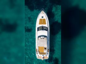 A stunning aerial view of a sleek yacht cruising over crystal-clear waters, showcasing its elegant design and spacious sunbathing area.