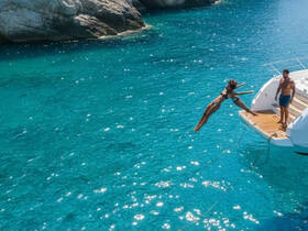 A woman joyfully leaps from the back of a boat into the stunning turquoise waters, capturing the essence of summer fun and adventure on the water.