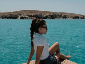 A woman relaxes on the edge of a boat, enjoying the stunning turquoise waters and scenic island backdrop — a perfect moment for tranquility on the water.