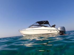 A person enjoys swimming in clear turquoise waters next to a stylish bow rider boat, creating a perfect scene for summer adventures on the water.