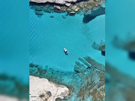 Aerial view of a small boat navigating through crystal-clear turquoise waters, surrounded by rocky shores — a perfect scene for exploring hidden coves and enjoying the beauty of nature.