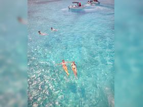 Two friends enjoy a refreshing swim in crystal-clear waters while a boat passes by, capturing the essence of a perfect day on the water.