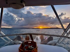 A couple enjoys a serene sunset aboard a boat, capturing the perfect moment of relaxation with drinks in hand — an ideal scene for romantic getaways.