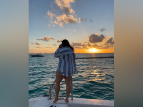 A woman enjoys a stunning sunset while standing on the deck of a boat, capturing the serene moment with a phone call — perfect for sunset cruises and memorable experiences on the water.