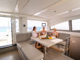 Three friends enjoy a relaxing moment inside a stylish boat cabin, complete with a dining area and refreshments, perfect for socializing on the water.